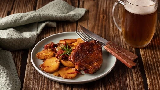 Grilovaná krkovice s bramborami a pivem na talíři.