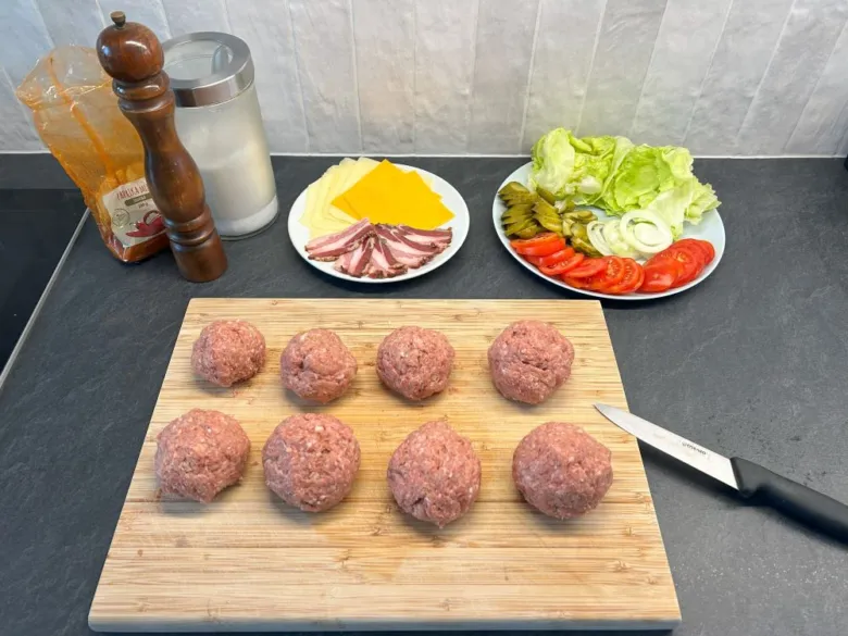 Surové hovězí burgery s přílohami na dřevěném prkénku.