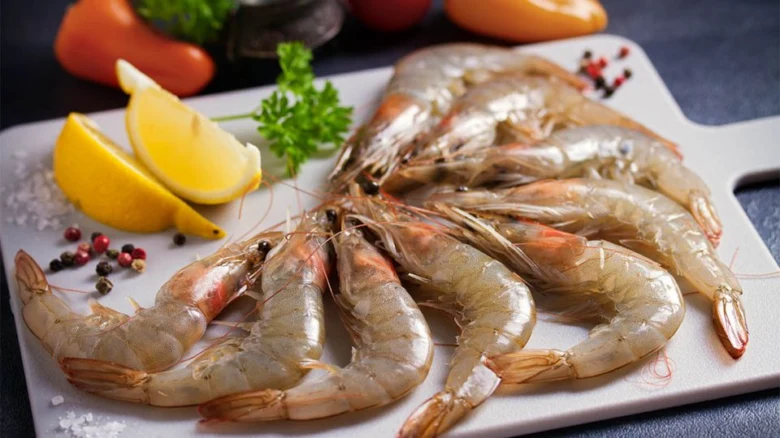 Surové krevety na bílém prkénku s citronem a kořením.