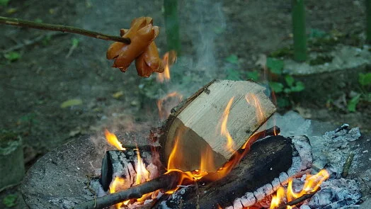 Klobásy se grilují nad ohněm venku.