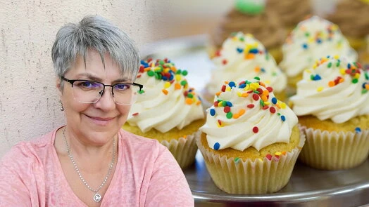 Usmívající žena s muffiny posypané barevnými cukrovinkami.