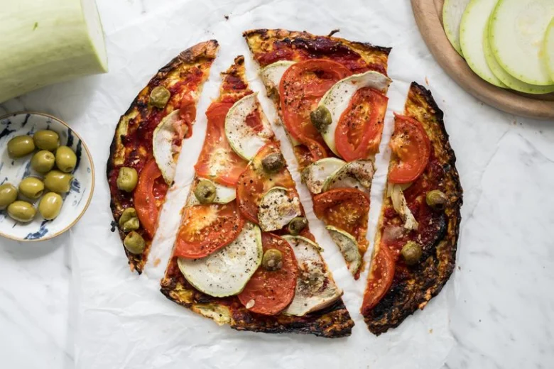 Hotová cuketová pizza s rajčaty bez mouky na bílém podkladu.