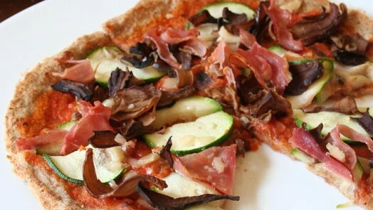 Domácí pizzy s cuketou, houbami a šunkou na bílém talíři.