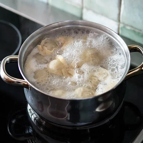 Pelmeni se vaří v hrnci s vroucí vodou na sporáku.