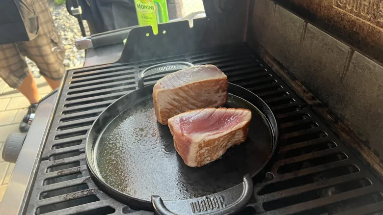 Dva kusy tuňáka se smaží na pánvi nad otevřeným ohněm grilu.