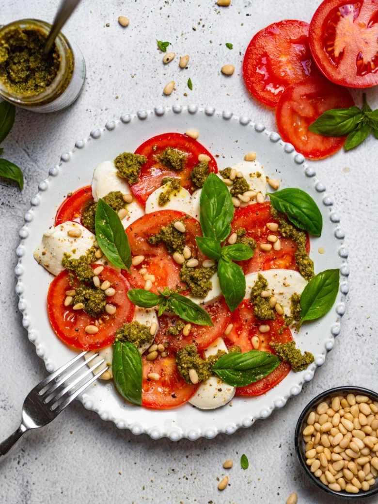 Caprese salát s rajčaty, mozzarellou, bazalkou, pestem a piniovými oříšky.