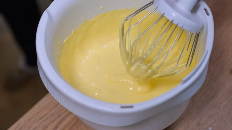 Bílý mixér míchá žluté těsto v bílé misce.