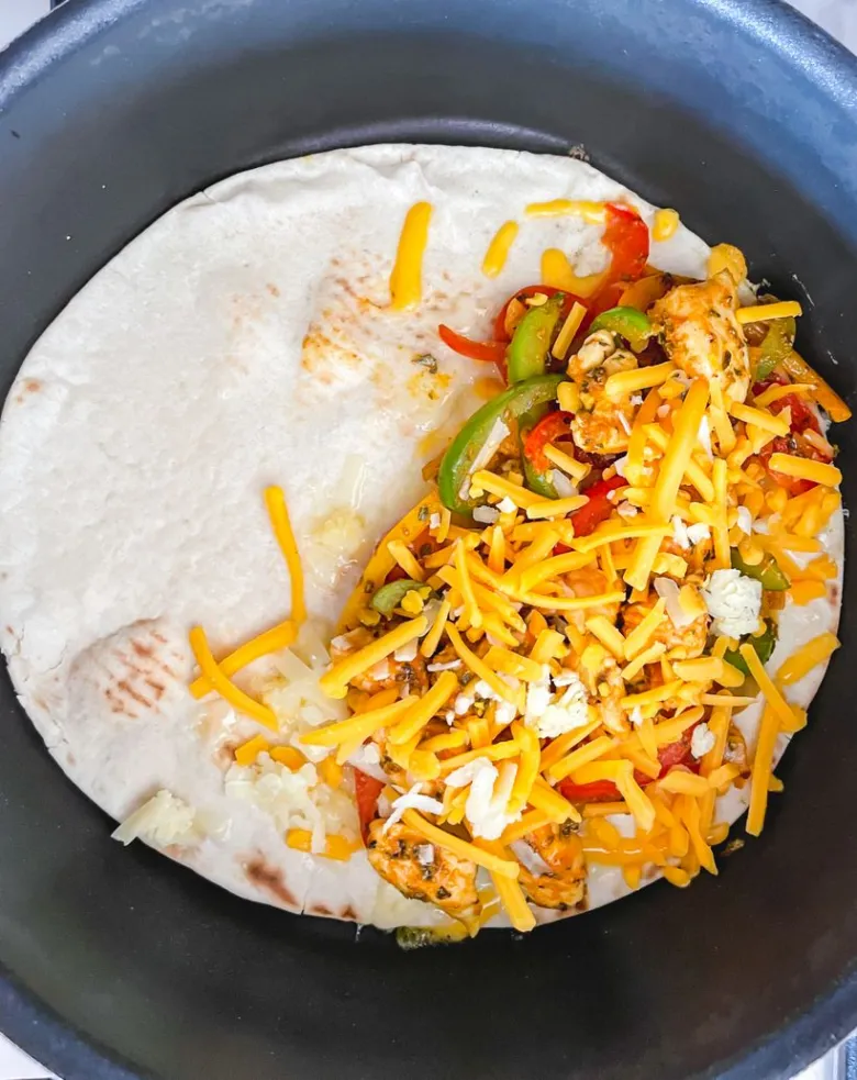 Tortilla s kuřecím masem, zeleninou a sýrem v pánvi.