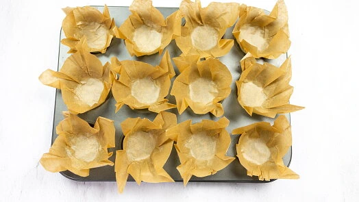 Tray s dvanácti papírovými formičkami na muffiny připravený k pečení.