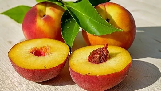 Čerstvé meruňky s listy na dřevěném povrchu.