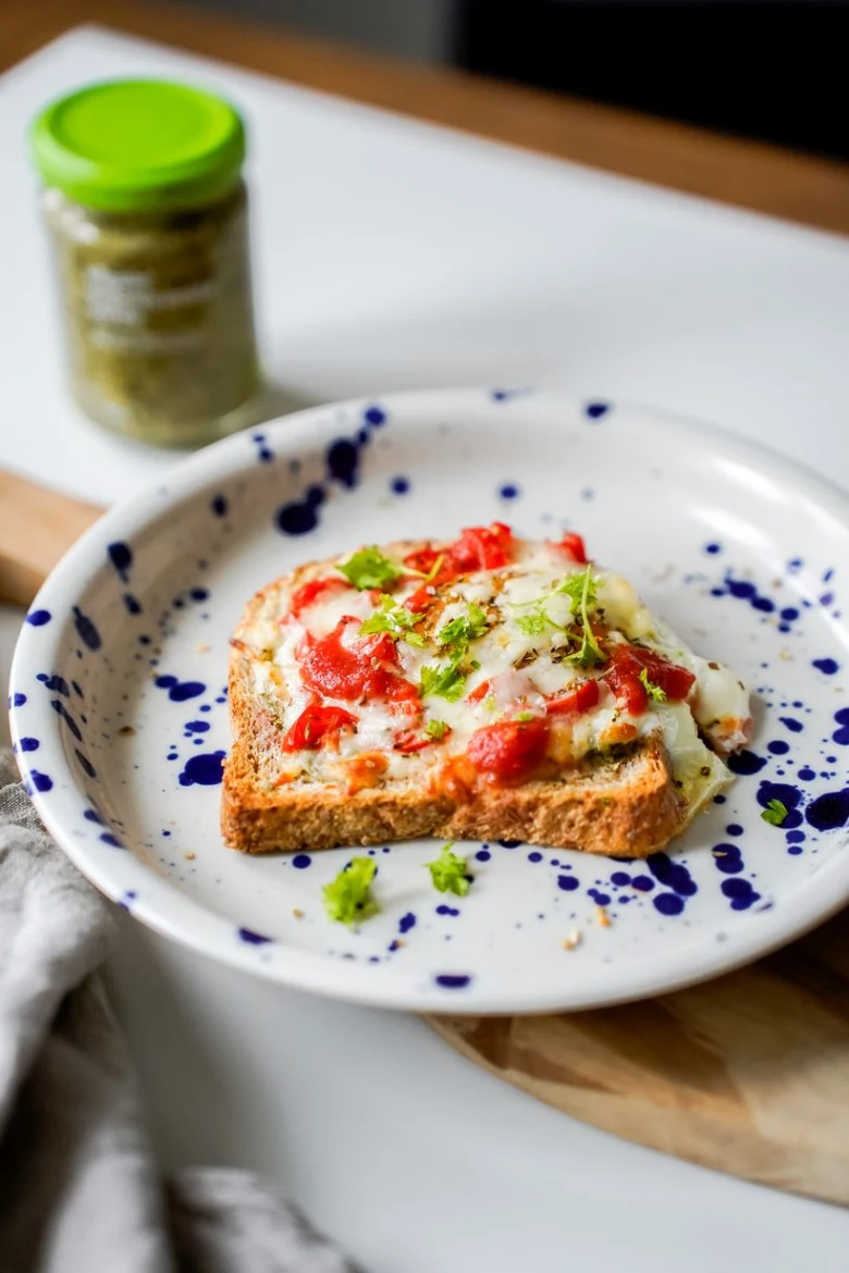 Zapečený toast s rajčaty, sýrem a bylinkami na talíři.