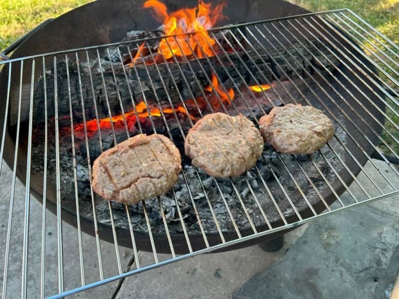 Tři hovězí burgery se pekou na roštu nad uhlím.
