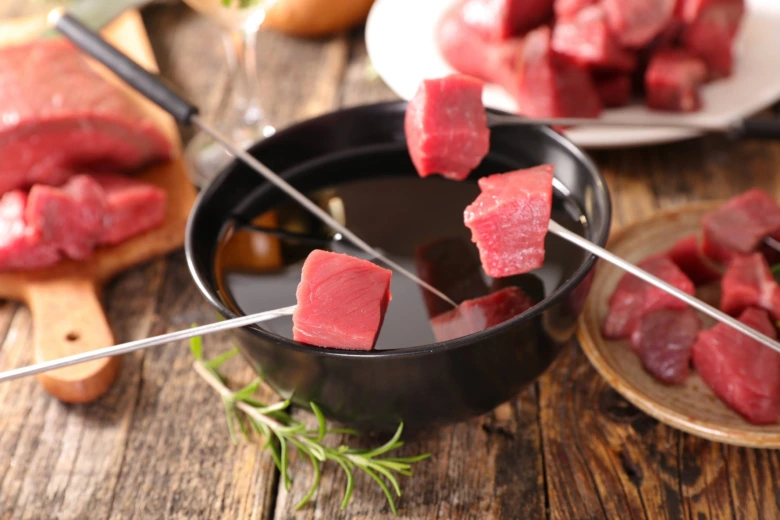 Česká fondue s kousky masa na špejlech v černé misce.