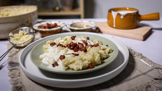 Položka s haluškami, brynzou a křupavým masem na talíři.