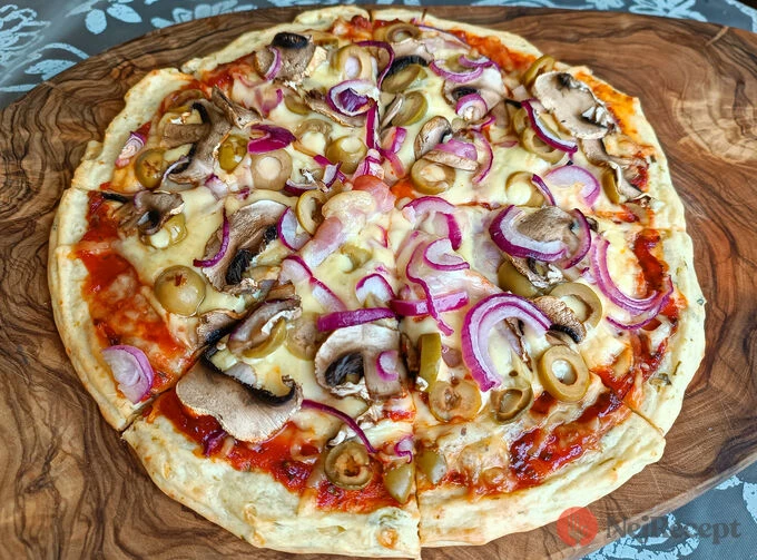 Domácí pizza s houbami, cibulkou a olivami na dřevěném talíři.