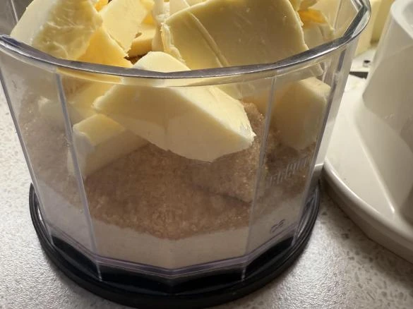 Kusy másla na hnědém cukru v mixéru pro bezpečení cheesecake.