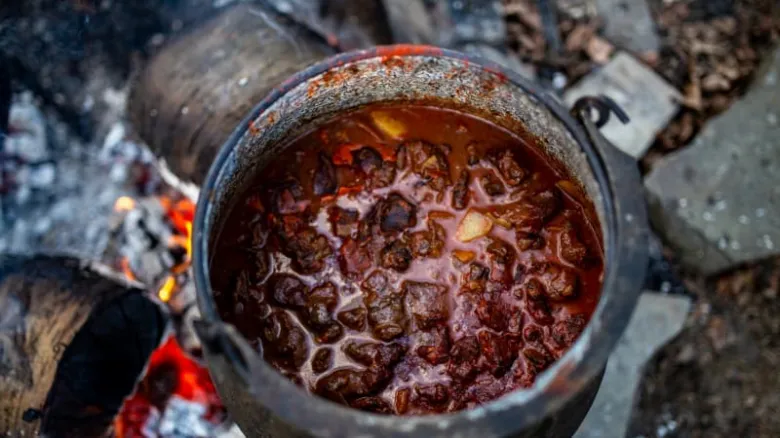 Hot segedínský guláš vařící v hrnci nad ohněm.