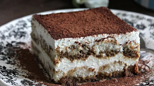 Kousek tiramisu s vrstvami sušenků, krému a kakaa na talíři.