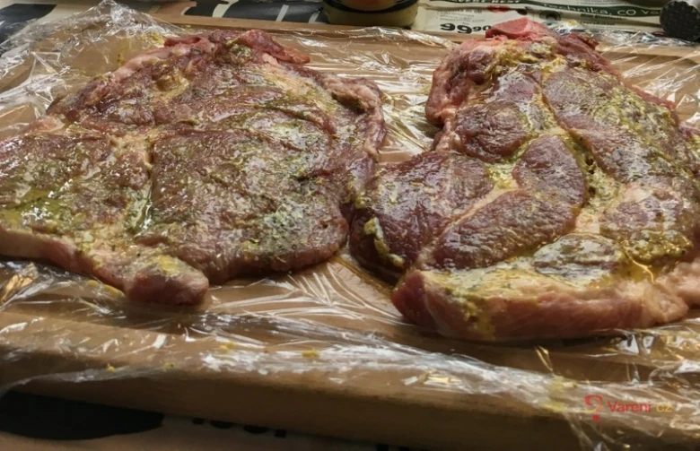 Dvě vepřové krkovice marinované s bylinkami na dřevěném prknu.