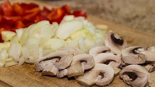 Nařezané zelenina: paprika, cibule a houby na prkénku.