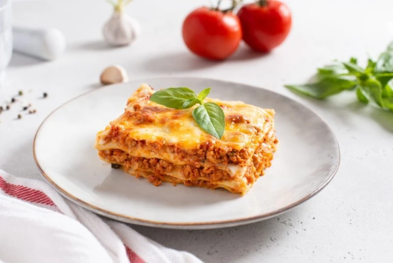 Kousek pečené lasagne s bazalkou na talíři.