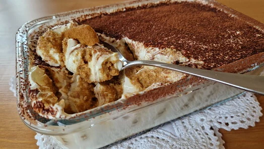Italské tiramisu v skleněné míse s lžící a kakaem.