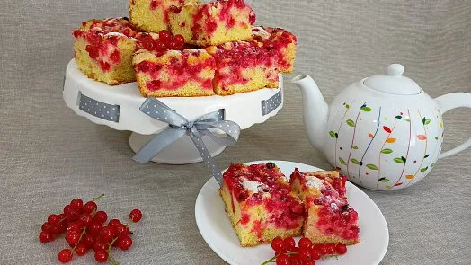 Kusky tvarohového koláče s rybízem na bílém podstavci.