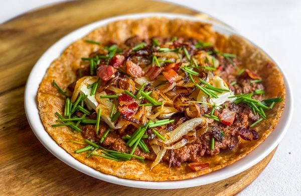 Připravená tortilla s masem, cibulí a bylinkami na bílém talíři.