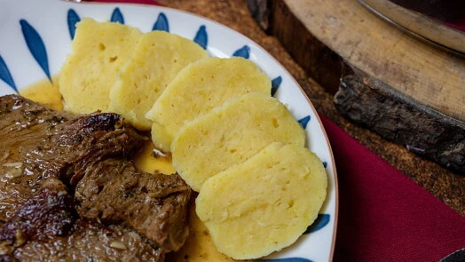 Domácí bramborové knedlíky podávané s masem na talíři.