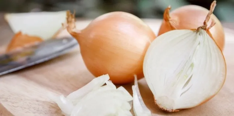 Celé žluté cibule s nakrájenou polovinou na dřevěném prknu.