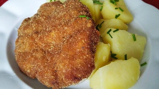 Zlatě opečený řízek s bramborami na bílém talíři.