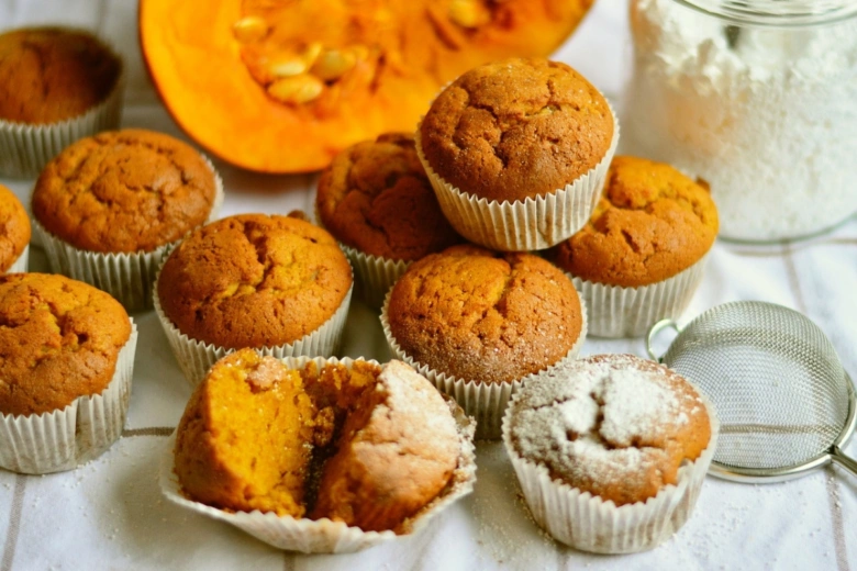 Svěží dýňové muffiny s moukou a sítkem na bílém povrchu.