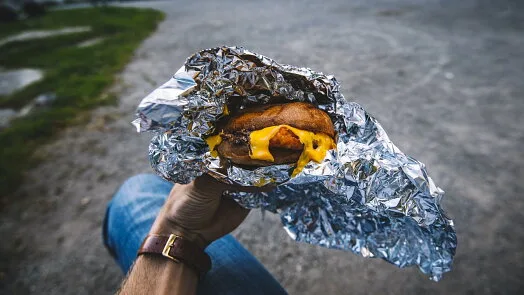 Ruce drží burger v hliníkovém fólii venku.