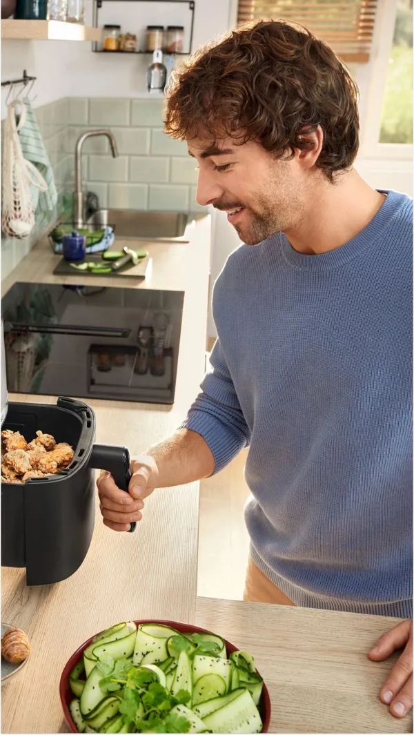 Muž drží otevřenou fritézu s kuřecím masem v kuchyni.