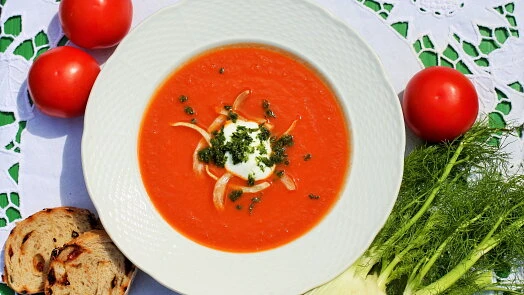 Mísa rajské polévky s kysanou smetanou a čerstvými ingrediencemi.