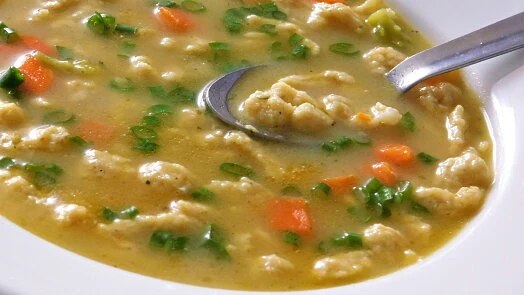 Hot Czech dumpling soup with vegetables and herbs in a serving bowl.